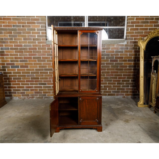 An English mahogany bookcase from the 19th century with glass doors, carved rosettes and acanthus leaves. Born in England...
