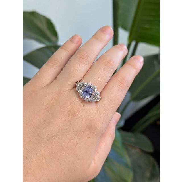 A cornflower blue sapphire sits in a soft cornflower blue at the heart of this solid 14K white gold ring, framed by sixty...