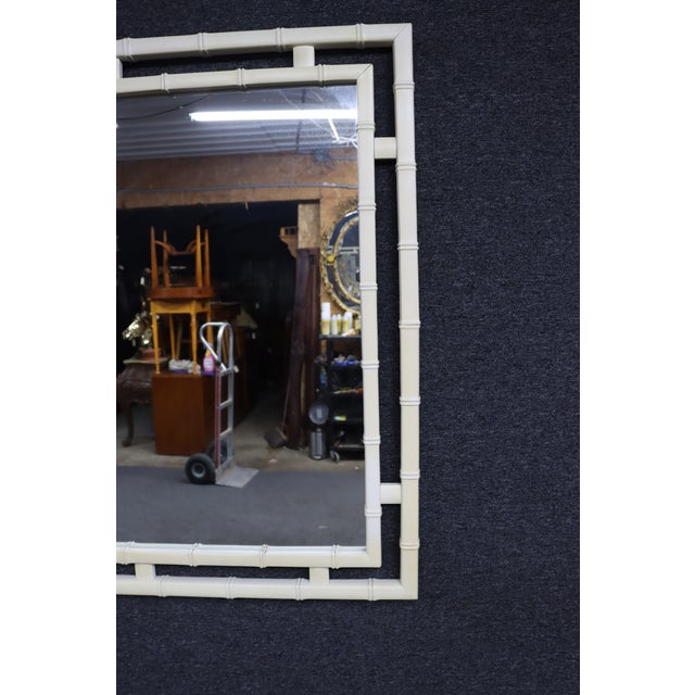 Hollywood Regency wall mirror featuring a faux bamboo frame in an ivory finish with a layered geometric design. The clean...