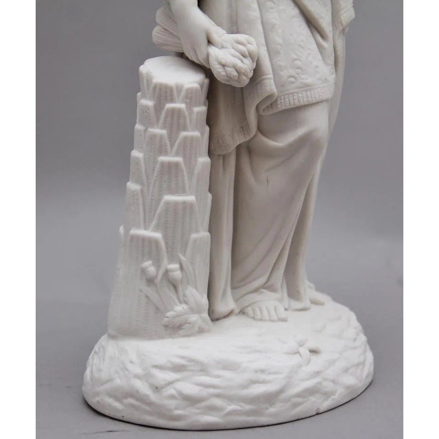 19th Century parian figure of a lady leaning on a column, here she is dressed in typical fashion of her time, holding what...