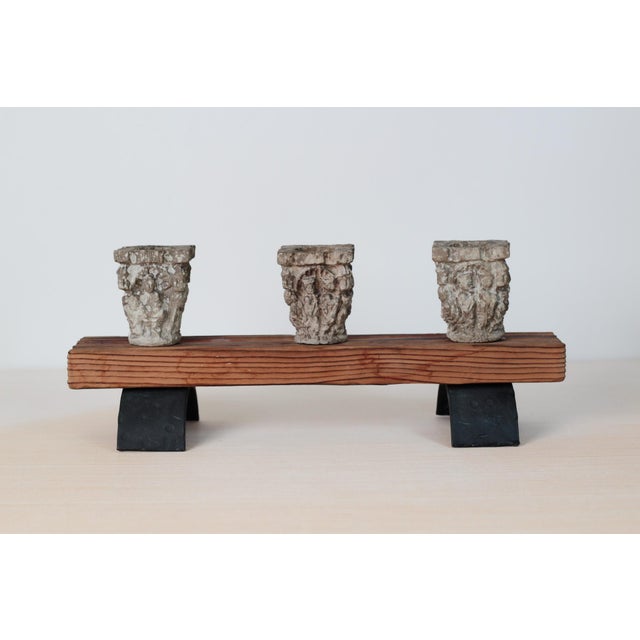 A striking architectural candleholder with three cast-plaster capitals in detailed relief, mounted on a rustic solid wood...