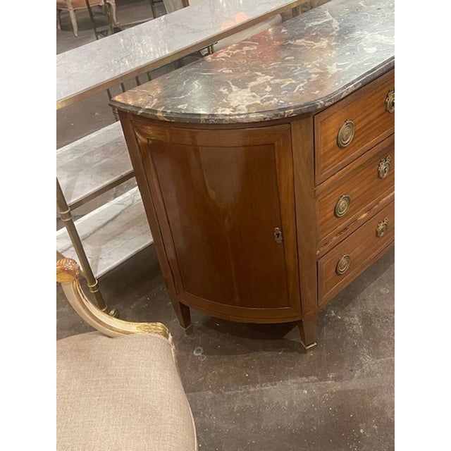 This French Louis XVI walnut demi-lune side cabinet is an exquisite antique piece that exudes elegance and sophistication....