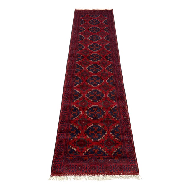 Repeating navy medallions create a bold geometric pattern across the rich red field of this tribal runner. Smaller motifs,...