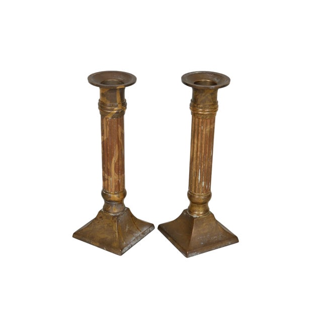 A pair of traditional candlestick holders made of brass. Simple wax pans top straight reeded columns above square bases....
