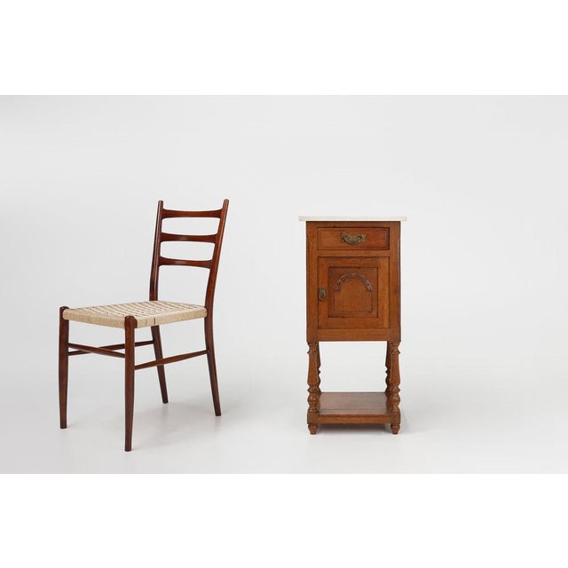 An exquisite Art Deco nightstand on graceful high legs in oak with carrara marble top. Crafted in France in the 1930s in...