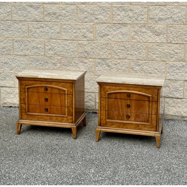 A pair of nightstands featuring three drawers elegantly accented with brass details and crafted from rich burled wood....