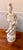 This statue of Guan Yin holding a lotus flower and standing in an elaborately carved base of lotus leaves and blossoms is...