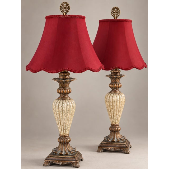 A matched pair of neoclassical table lamps with tall, fluted urn bodies in a cream crackle finish. Sculpted bronze-tone...
