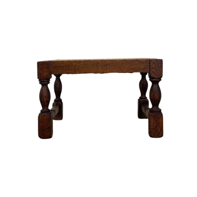 Crafted from solid dark oak, this vintage footstool features a traditional hand-woven cane top supported by elegant turned...
