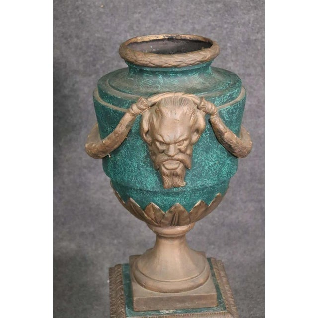 A pair of verdigris painted iron garden urns with bearded face and garland motif.