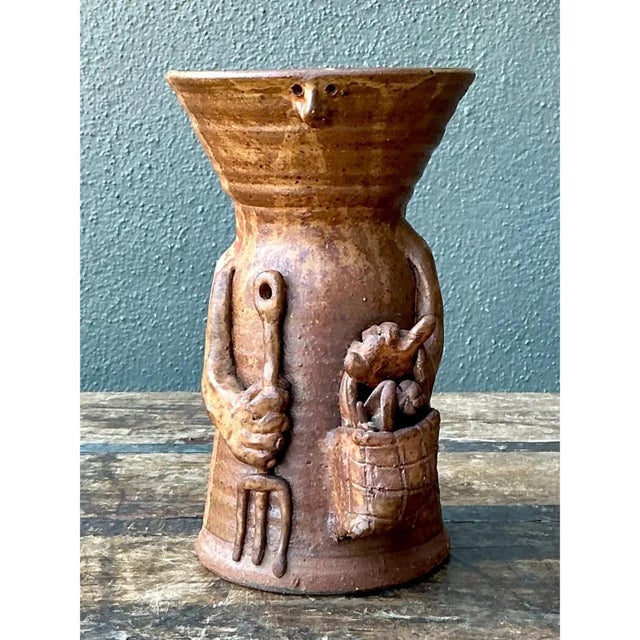 This stoneware vase presents a charming, narrative-driven design, its cylindrical body flaring outward at the top into a...