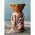 This stoneware vase presents a charming, narrative-driven design, its cylindrical body flaring outward at the top into a...