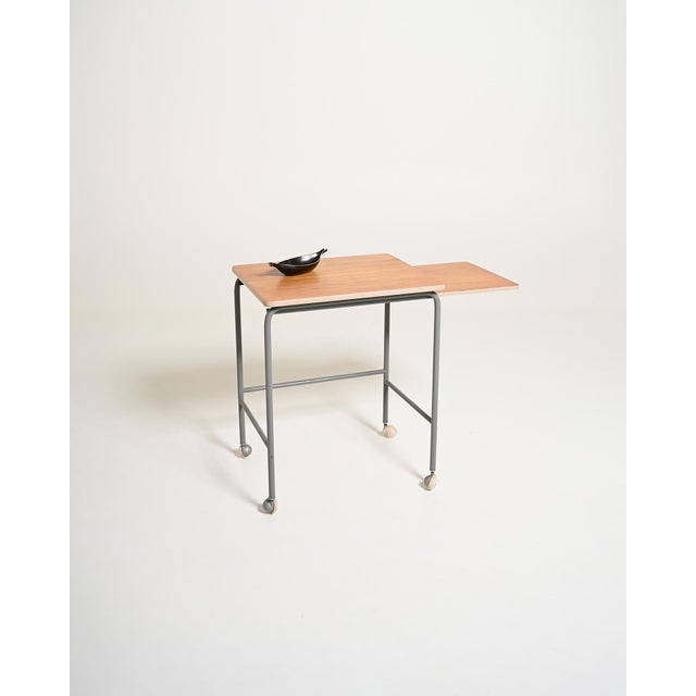 Coffee table on casters with a removable side shelf, tubular metal frame, and teak-covered tops. Original label present....