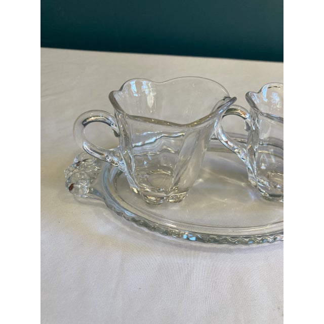 A charming vintage three-piece clear glass cream and sugar set featuring a matching creamer, open sugar bowl, and...