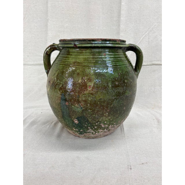A substantial hand-thrown earthenware jar with a luminous green glaze applied over a pale slip, revealing soft white...
