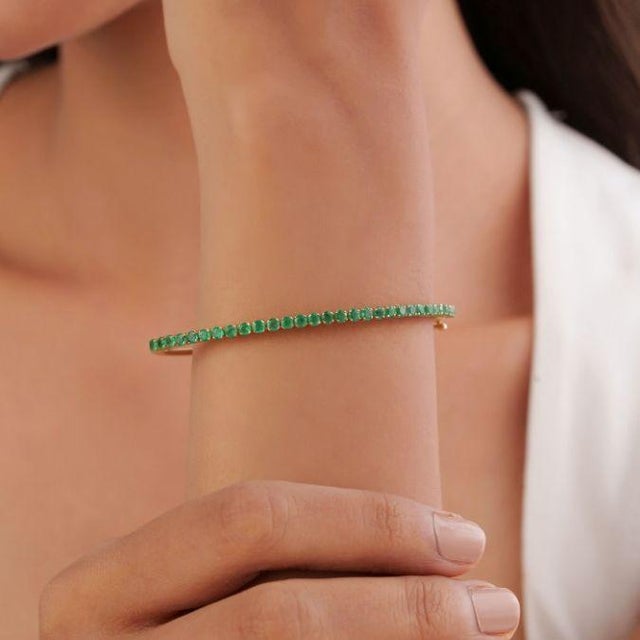 This elegant bangle features 1.86 carats of natural round cut emerald, set in 14k yellow gold. Each emerald measuring...
