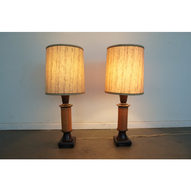 These vintage table lamps date to the mid-20th century and feature sculptural dark-stained wood bases with woven rattan...