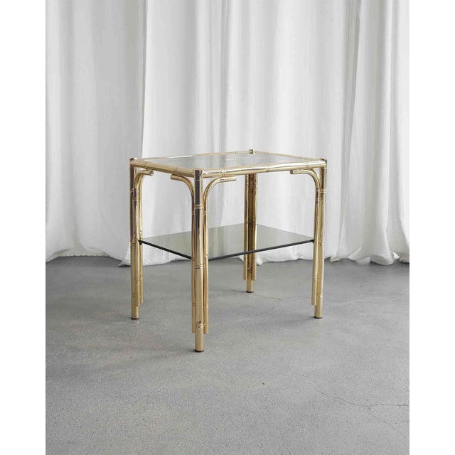 French brass side table made of bamboo-like frame shape. The table has two shelves made of smoked glass.‍
