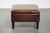 A large dark brown square ottoman made of sheepskin with black piping. : A sheepskin footstool, also known as an ottoman,...