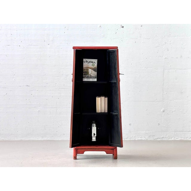 A striking, narrowly proportioned chinese wedding cabinet with a vibrant red lacquer finish and traditional-style metal...