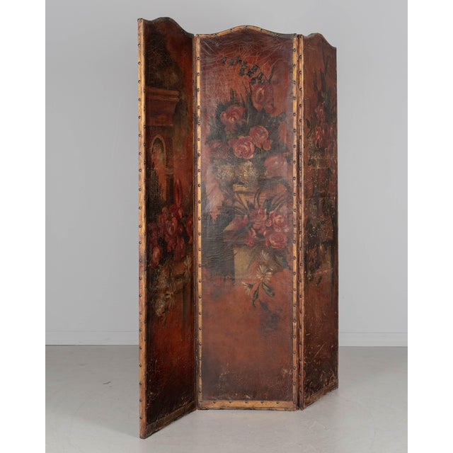 A Spanish Baroque style leather three panel folding screen, hand-painted in rich warm shades of red and brown with large...