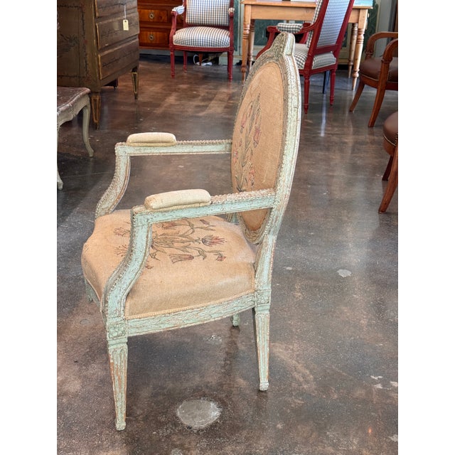 An 18th century Swedish armchair in worn pale blue-green paint, the oval back with a laurel-carved frame and rosette crest...