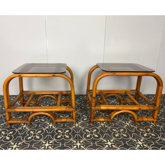 Stylish Italian pair of vintage mid-century modern bohemian bamboo-and-rattan side tables with dark, smoked glass tops....