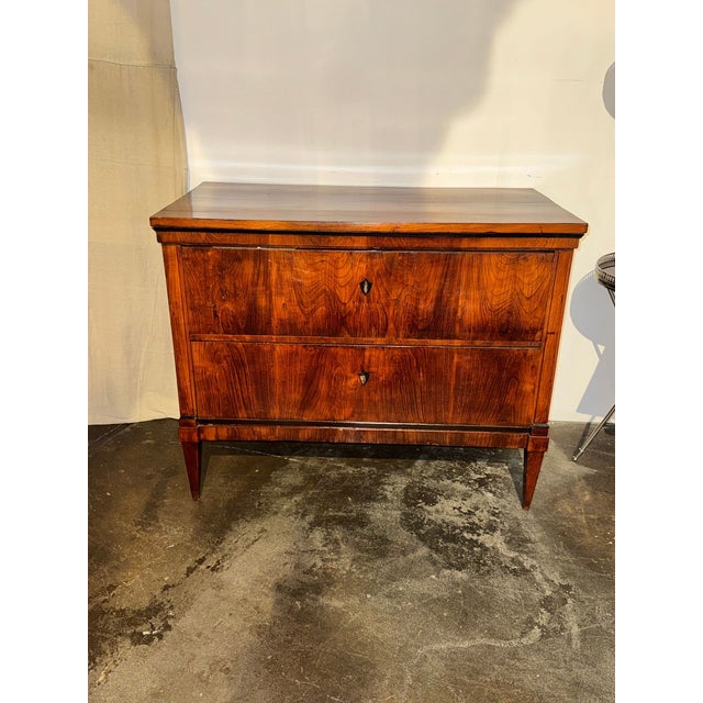 The product is an antique German Biedermeier walnut commode from the 19th century. This dresser or chest of drawers exudes...