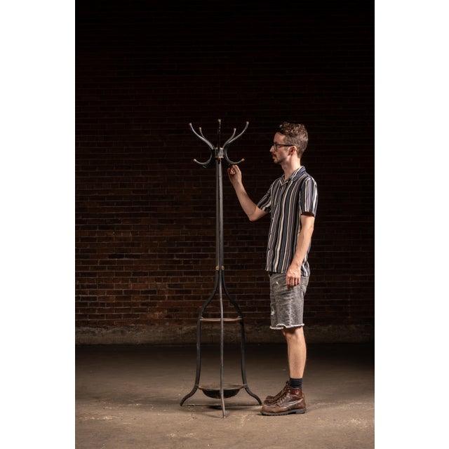 Cast iron hall tree featuring a revolving crown with eight outward-curving coat and hat hooks, each fitted with brass or...