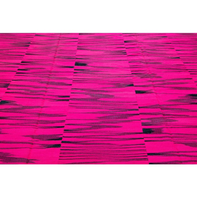 This contemporary Turkish kilim rug, crafted in the 21st century, features a vibrant highlighter-pink field adorned with...