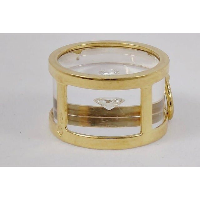 An avant-garde 1970s 18k pendant with a suspended brilliant-cut round diamond inside a cylinder of clear resin, framed in...