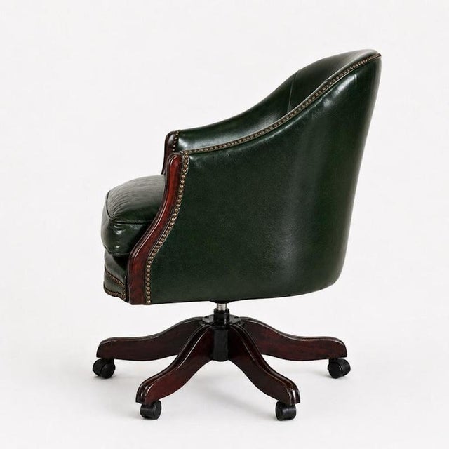 A handsome vintage swivel desk chair upholstered in richly toned racing green leather, with a rounded tub-form back,...