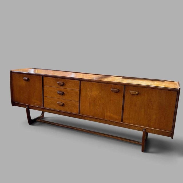 A striking mid-century teak long sideboard by Portwood, distinguished by an unusual sculptural sleigh-leg base and an...