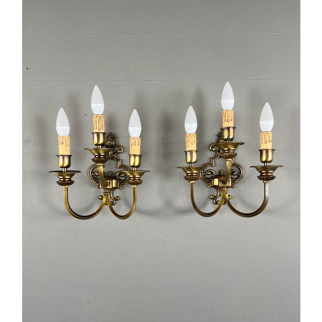 Elegant pair of brass wall sconces with finely crafted decoration and three lights. Each sconce features a curved...