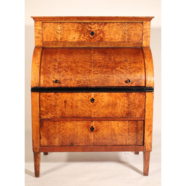 Biedermeier birch cylinder desk, circa 1830. With a black lacquered rectangular top, below is a drawer with a shield...