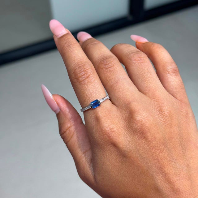 This Solitaire Ring showcases a 0.56 carat natural emerald-cut blue sapphire, set in 14k white gold. The sapphire...