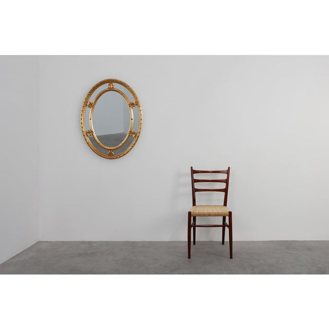 This 20th‑century oval mirror by Deknudt reflects the refined elegance of Neo‑Classical design, interpreted through the...