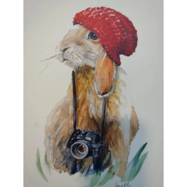 Charming bunny art print featuring a red hat and vintage camera. Soft watercolor tones and green accents create a cozy,...