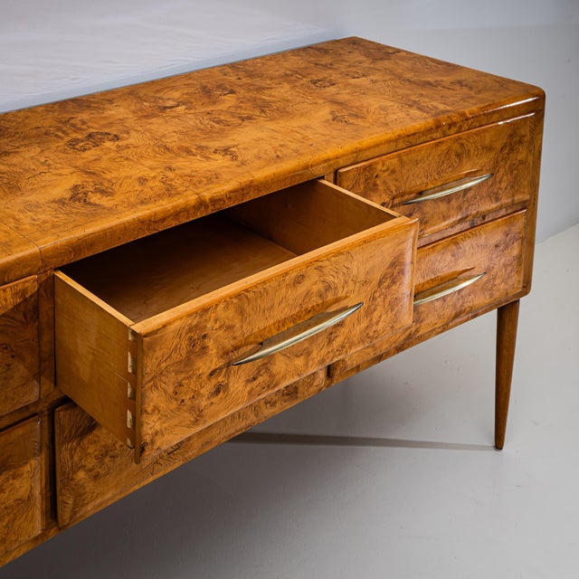 Elegant sideboard featuring a gently concave front, six drawers with long horizontal brass handles, and slender tapered...