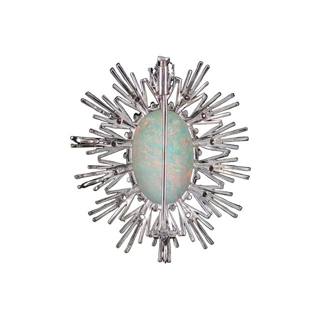 A striking mid-century brooch features a central approximately 10 carat opal. Surrounding the opal are 14 brilliant-cut...