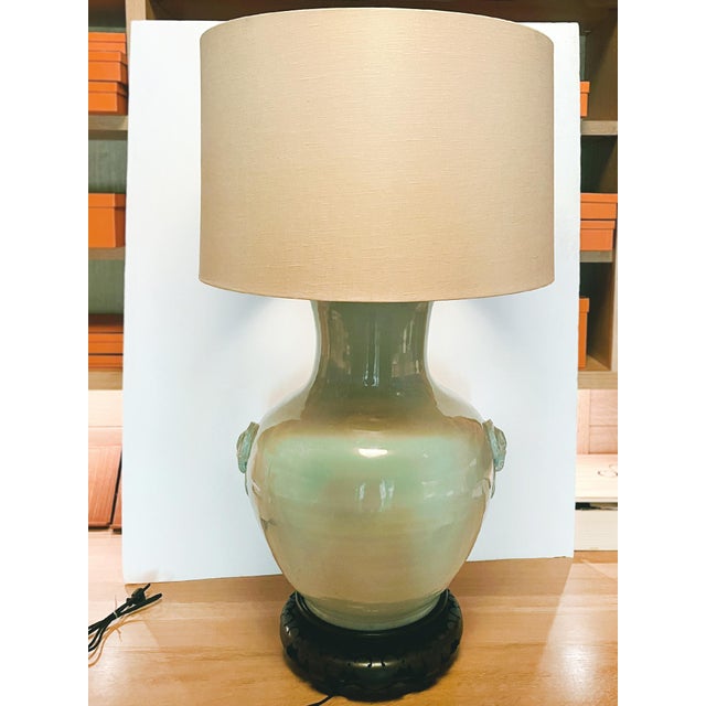 An elegant large table lamp consisting of a converted ceramic urn body in a celadon green glaze, an ebonized carved wooden...
