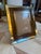 A tabletop picture frame with a richly patterned burl wood border, framed by warm brass trim on both the outer edge and...