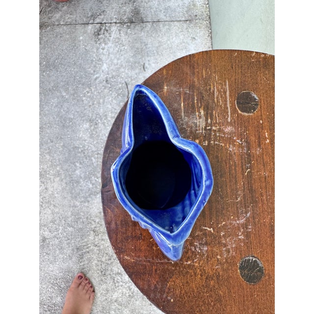 An artisanal cobalt blue ceramic pitcher in the form of a toucan, with generous spout and looped handle. The deep...