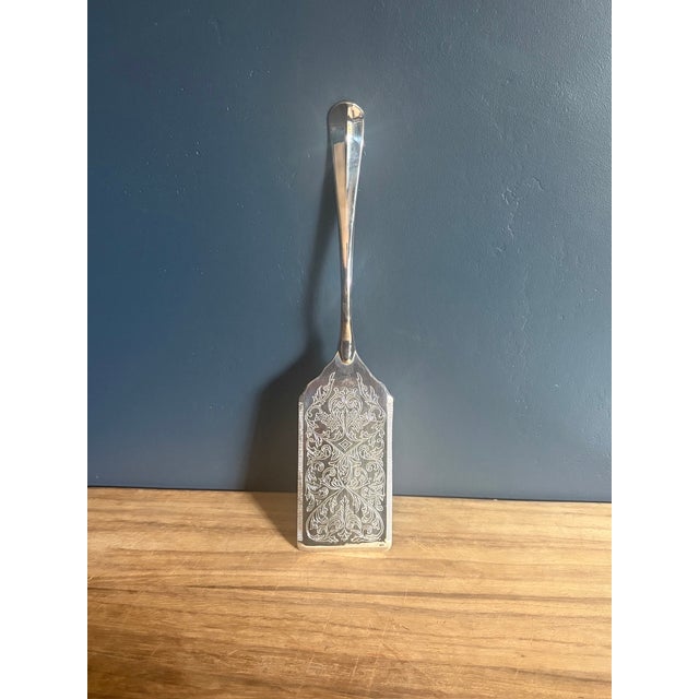 A cake and pastry server. The entire blade face is engraved with symmetrical foliate scrollwork framed by a fine linear...