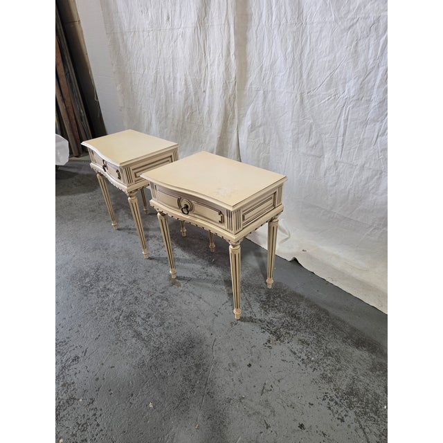 A charming pair of vintage Louis XVI-style nightstands featuring elegant fluted tapered legs, serpentine drawer fronts,...