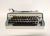 A 1960s Sherwood portable typewriter, made in Italy. The mid-century typewriter is blue and cream with a gray carrying...