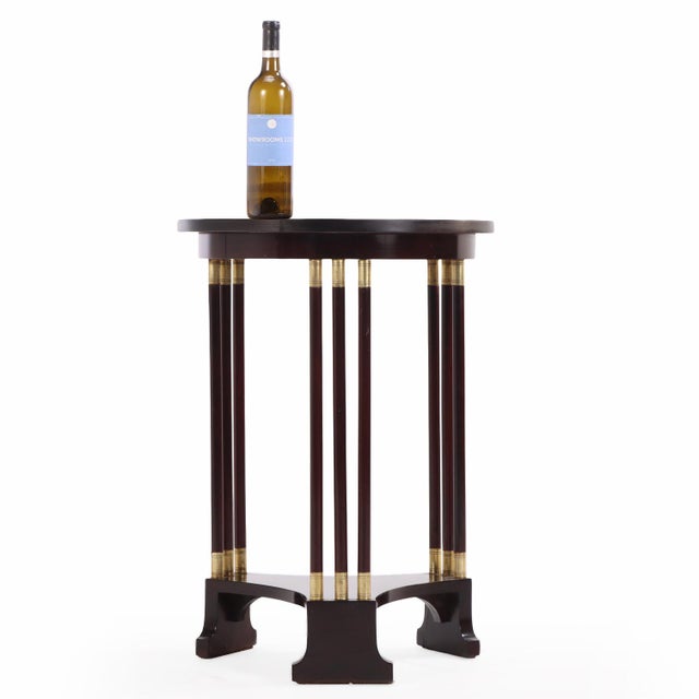 Crafted in mahogany and accented with bronze mounts, the table features a circular top above a shaped lower shelf, the...