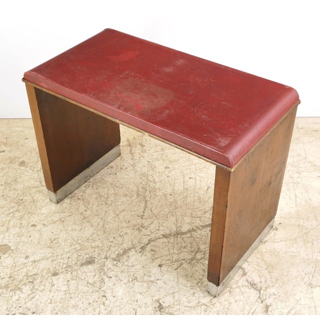 Art Deco style console table made of dark wood tone oak sides, a red vinyl top, and leg bases capped with steel. It...