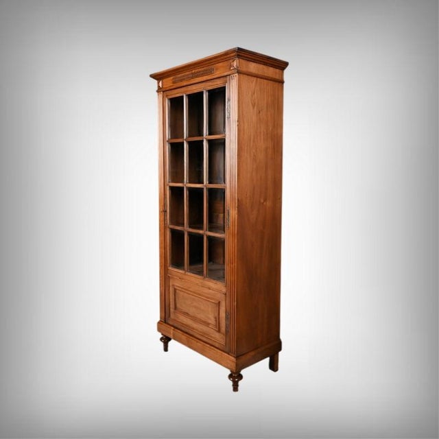 This Louis XVI-inspired walnut display cabinet is distinguished by its classic appearance, featuring a door adorned with...