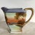 This Vintage Japanese Noritake Porcelain Creamer showcases a hand-painted pastoral scene, complete with soft sunset hues...